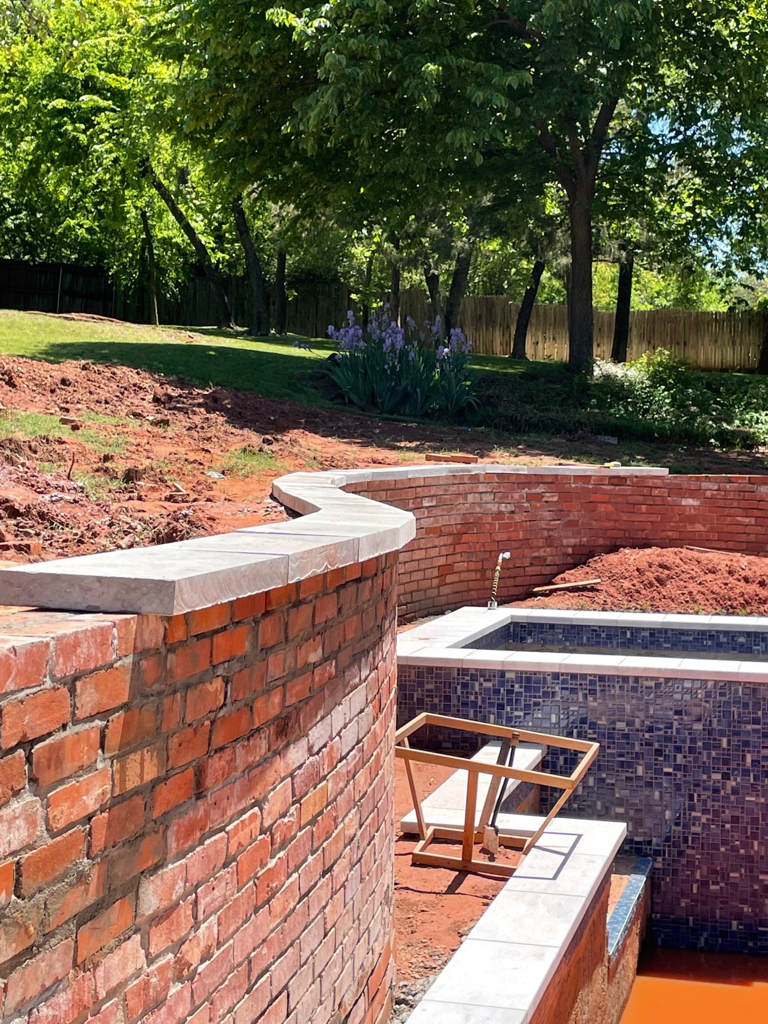 Curved brick retaining wall with limestone cap and mosaic tile pool shell under construction