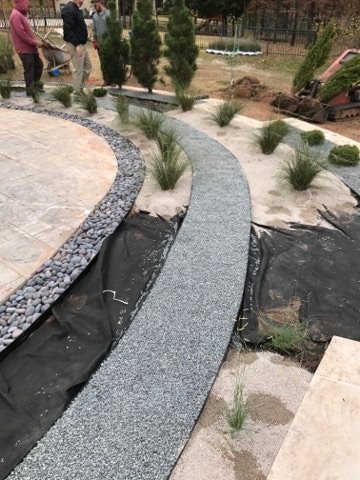 Curved gravel pathway installation with river rock border and ornamental grass plantings