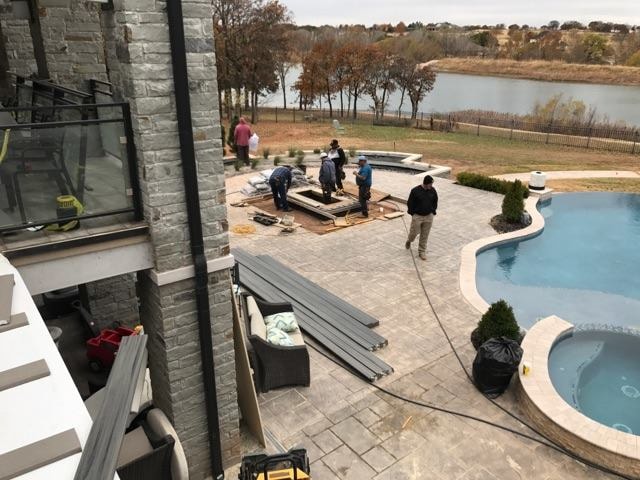 Crew installing outdoor kitchen structure on travertine paver patio overlooking lakeside pool