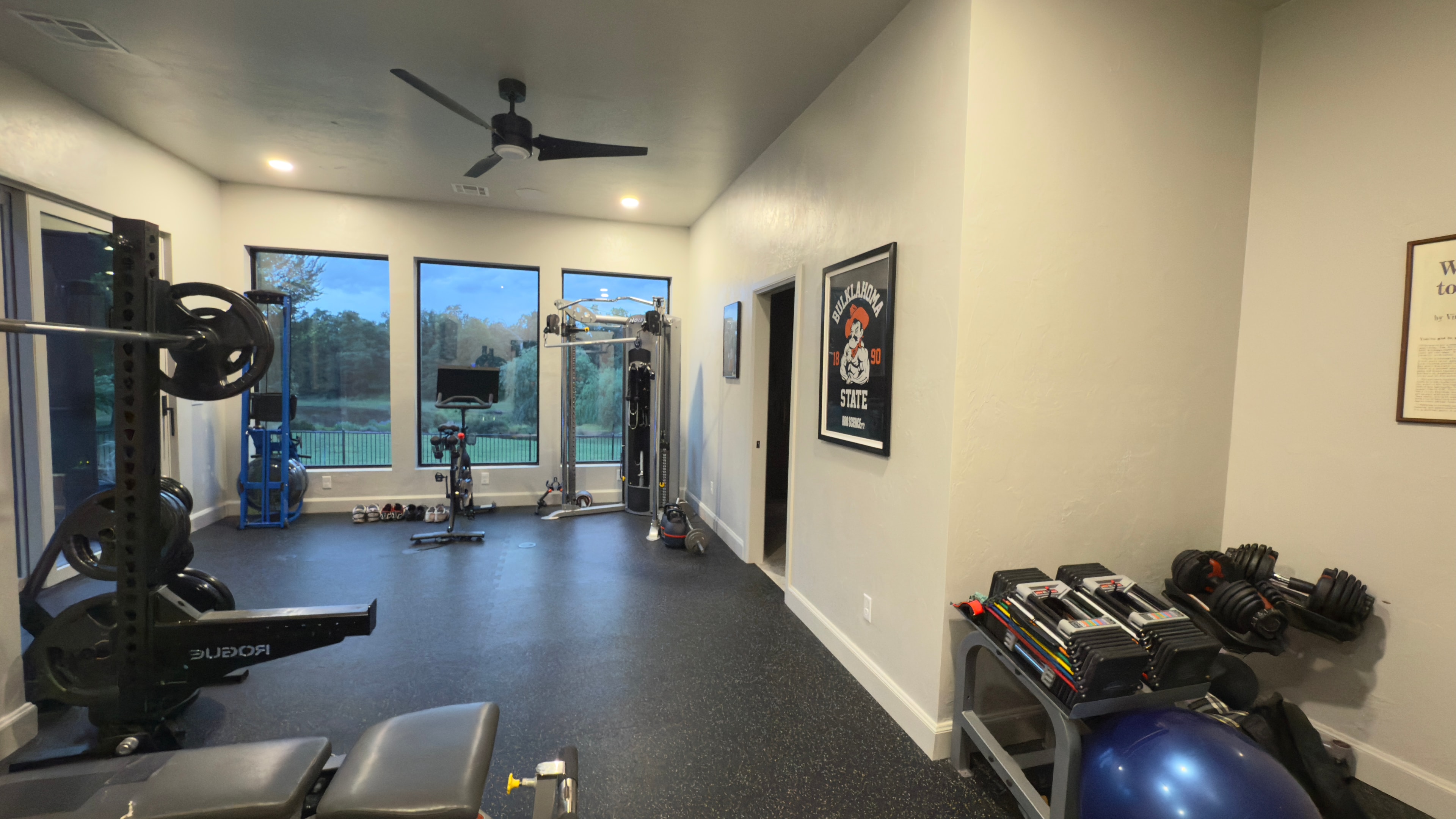 Custom home gym with Rogue rack, dumbbells, and pool views through large windows