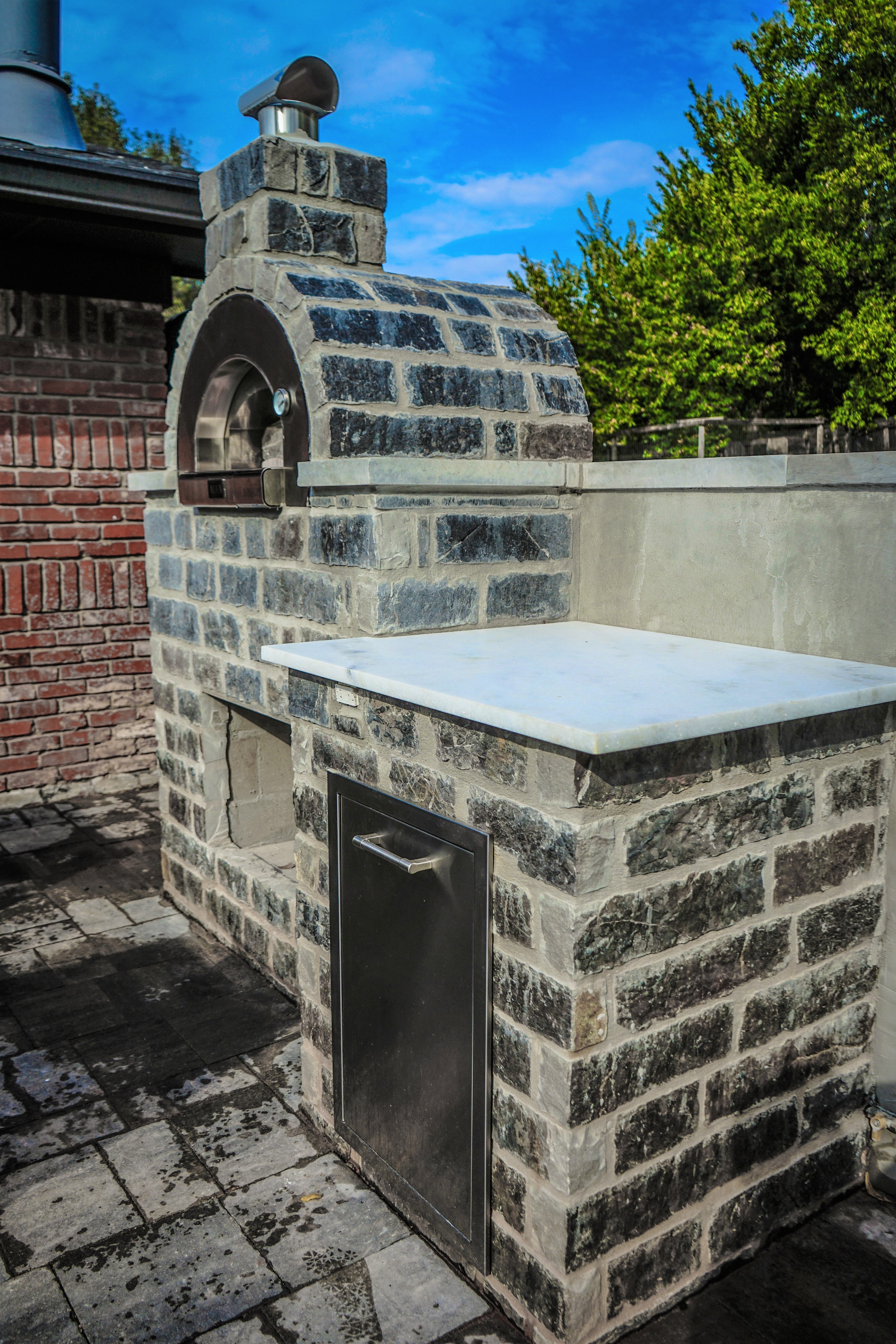 Covered patio outdoor kitchen with brick fireplace, granite bar top, and wrought-iron seating