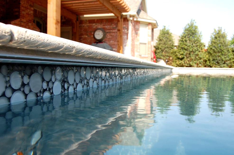 Close-up of pool waterline with custom round glass mosaic tile and stone coping