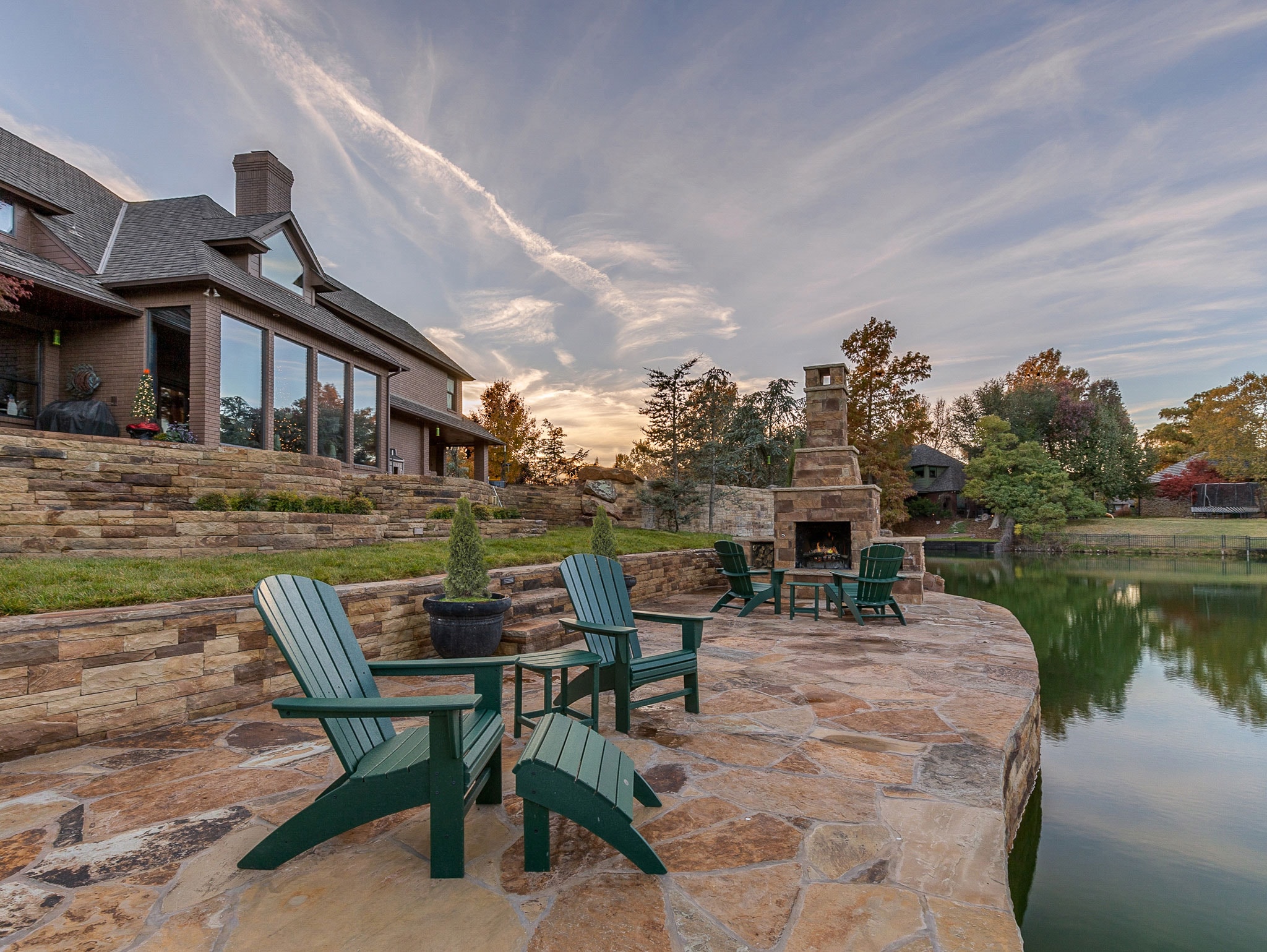 Wide-angle view of flagstone patio with fireplace, Adirondack seating, and pond at dusk